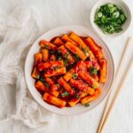 Tteokbokki Korean spicy rice cakes in gochujang sauce served in a shallow bowl garnished with green onions and sesame seeds