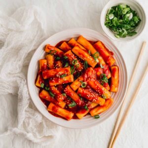 Tteokbokki Korean spicy rice cakes in gochujang sauce served in a shallow bowl garnished with green onions and sesame seeds