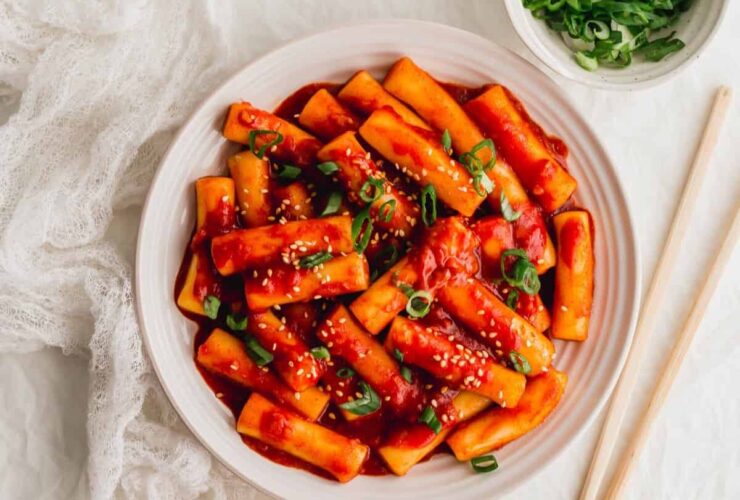 Tteokbokki Korean spicy rice cakes in gochujang sauce served in a shallow bowl garnished with green onions and sesame seeds