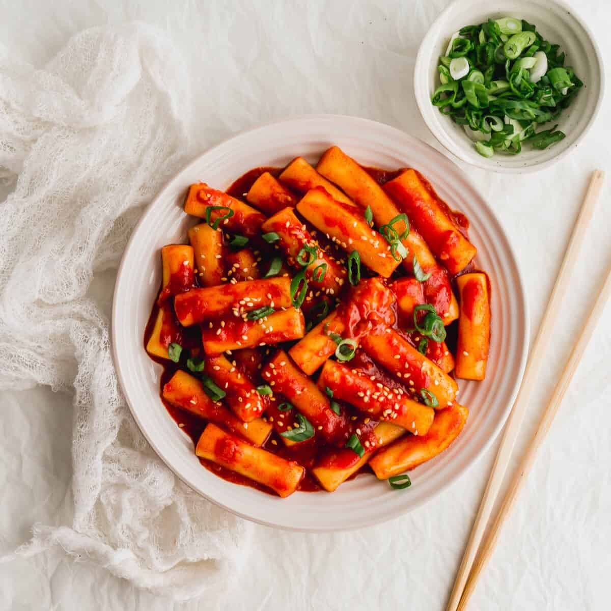 Tteokbokki Korean spicy rice cakes in gochujang sauce served in a shallow bowl garnished with green onions and sesame seeds
