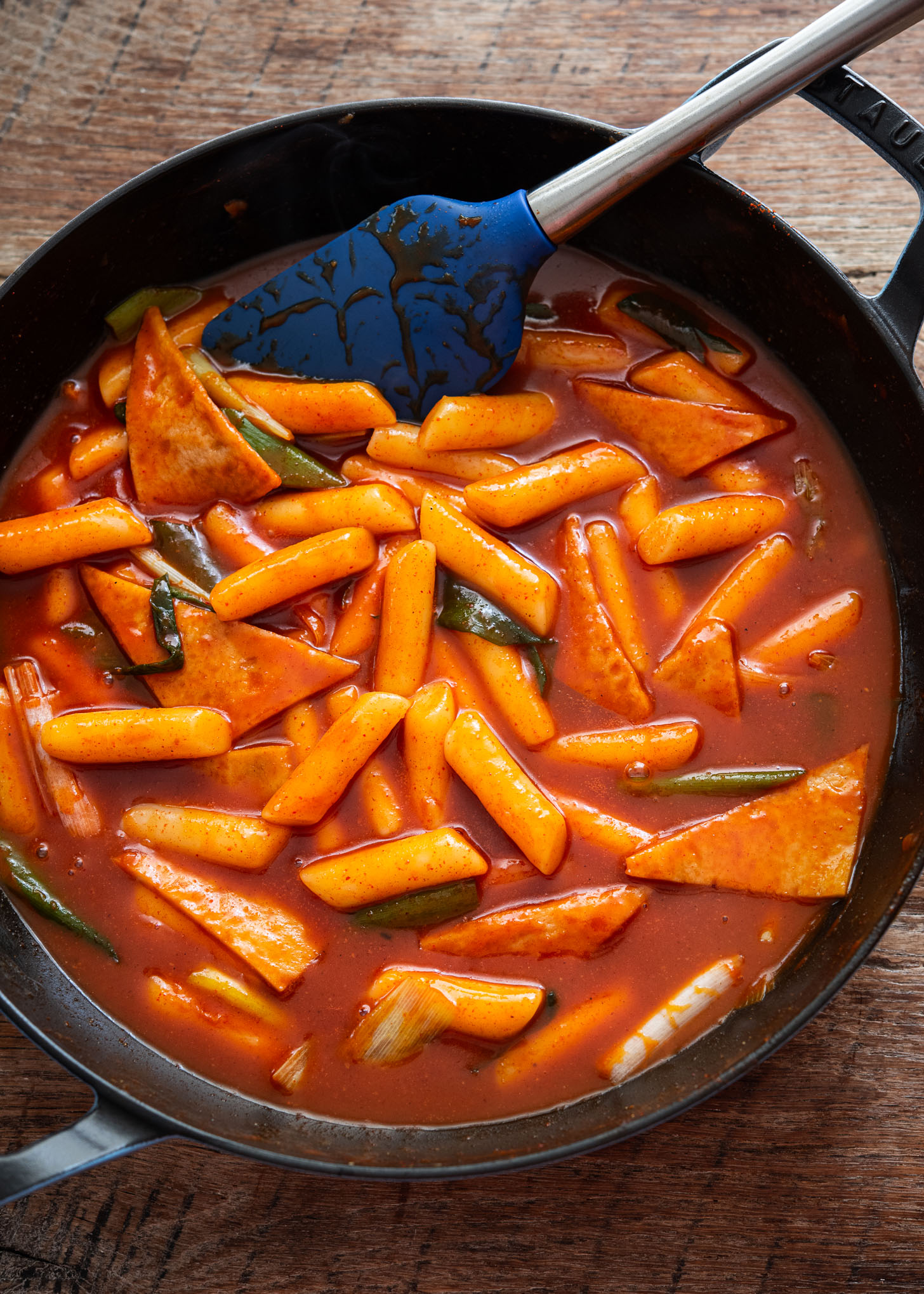 Tteokbokki ingredients flat lay including rice cakes, gochujang, fish cakes, green onions, and anchovy kelp broth on a marble surface