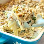 Creamy tuna casserole in a white baking dish with a golden breadcrumb topping, fresh parsley garnish, and a serving spoon resting on the side