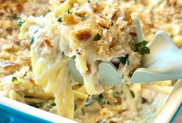 Creamy tuna casserole in a white baking dish with a golden breadcrumb topping, fresh parsley garnish, and a serving spoon resting on the side