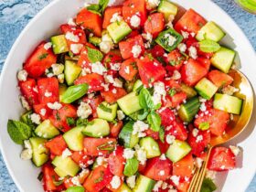 overhead flat lay of watermelon feta salad in a large white serving bowl with fresh mint, crumbled feta, sliced cucumber, and a honey-lime drizzle on a bright summer table
