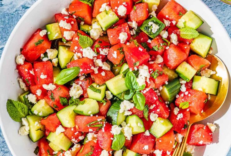 overhead flat lay of watermelon feta salad in a large white serving bowl with fresh mint, crumbled feta, sliced cucumber, and a honey-lime drizzle on a bright summer table
