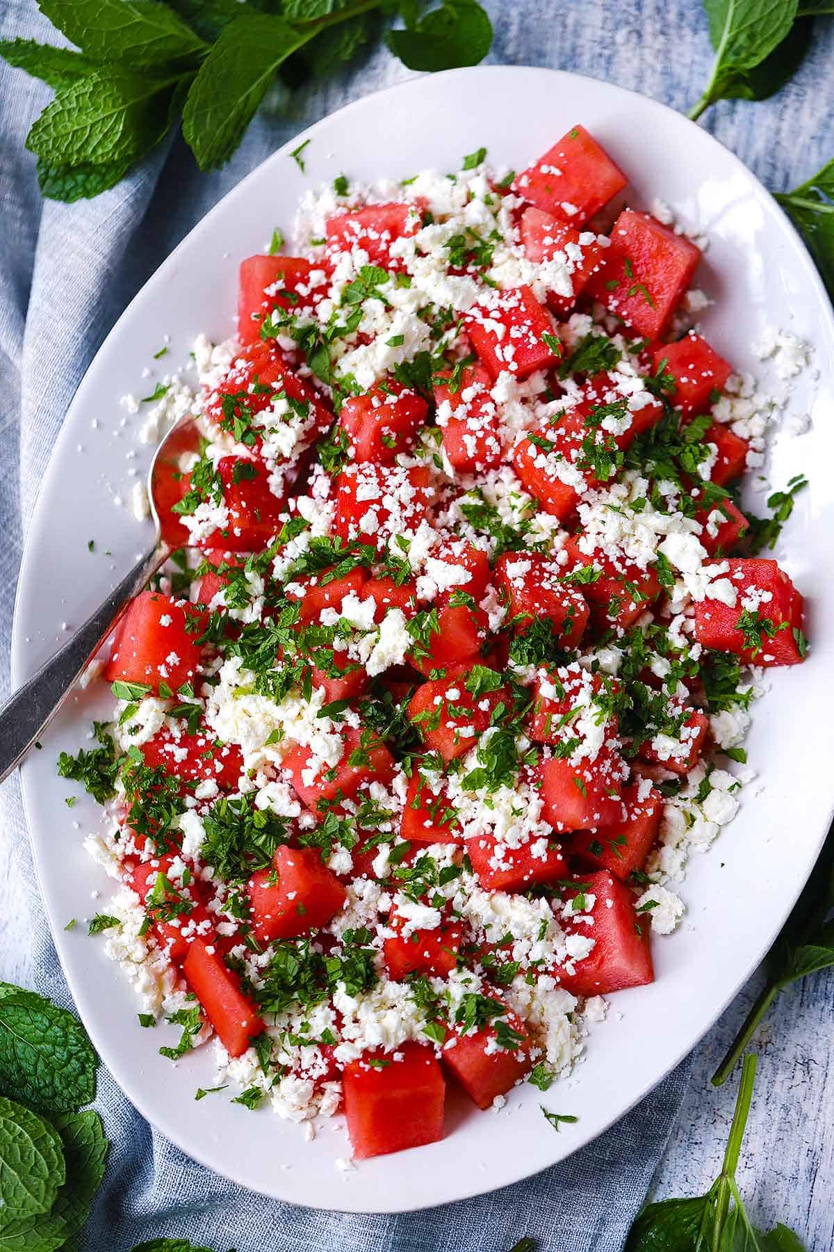 close-up shot of a serving of watermelon feta salad in a wide bowl showing the contrast of red watermelon, white feta crumbles, green mint leaves, and a glistening honey-lime glaze