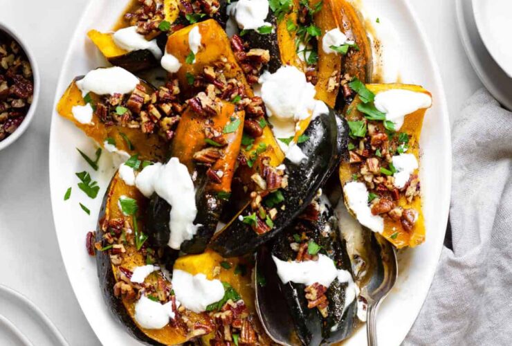 Close-up of a single air fryer acorn squash wedge with caramelized maple glaze, drizzled with white Greek yogurt sauce and sprinkled with cinnamon, on a dark ceramic plate