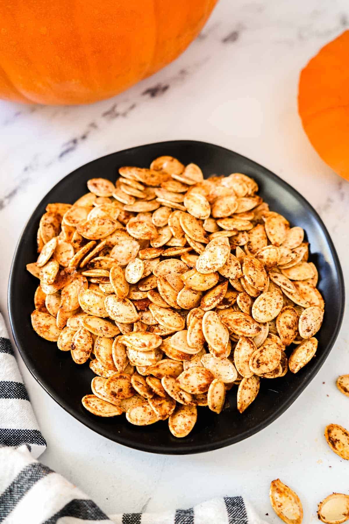 Air Fryer Pumpkin Seeds — Crispy, No-Oil Salted or Sweet Snack 12 Close-up of air fryer pumpkin seeds in a small white ceramic bowl, some seeds split open to show the golden interior, with cinnamon sticks and sea salt flakes as props
