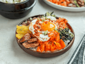 A beautifully plated Bibimbap Korean rice bowl with colorful sautéed vegetables, a sunny-side-up egg, and a drizzle of gochujang sauce, served in a stone bowl