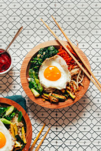 Overhead flat-lay of Bibimbap ingredients including sautéed spinach, julienned carrots, shiitake mushrooms, bean sprouts, ground beef, and gochujang sauce arranged around a bowl of rice
