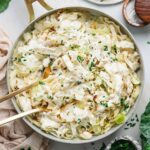 Cabbage Alfredo served in a wide shallow bowl with charred cabbage ribbons draped in creamy parmesan sauce, topped with cracked black pepper and fresh parsley, shot on a linen tablecloth with a fork resting on the side