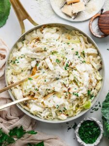 Cabbage Alfredo — Creamy Parmesan Sauce Over Charred Cabbage Ribbons 13 Cabbage Alfredo served in a wide shallow bowl with charred cabbage ribbons draped in creamy parmesan sauce, topped with cracked black pepper and fresh parsley, shot on a linen tablecloth with a fork resting on the side