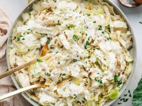 Cabbage Alfredo served in a wide shallow bowl with charred cabbage ribbons draped in creamy parmesan sauce, topped with cracked black pepper and fresh parsley, shot on a linen tablecloth with a fork resting on the side