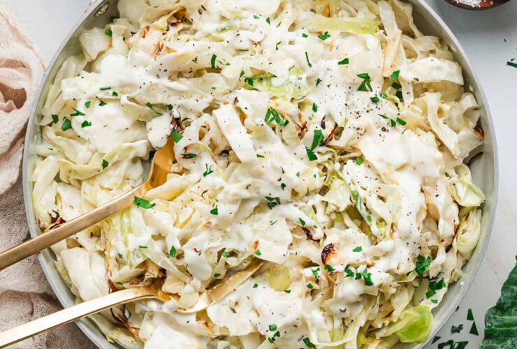 Cabbage Alfredo served in a wide shallow bowl with charred cabbage ribbons draped in creamy parmesan sauce, topped with cracked black pepper and fresh parsley, shot on a linen tablecloth with a fork resting on the side