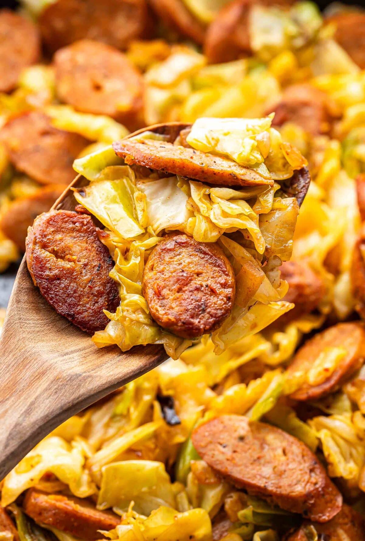 Close-up of caramelized cabbage and sausage skillet with golden-brown sausage coins nestled in wilted, golden cabbage, with a fork resting on the edge of the pan