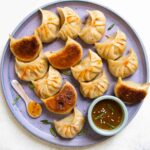 Crispy golden cabbage dumplings arranged on a plate with dipping sauce and fresh scallions