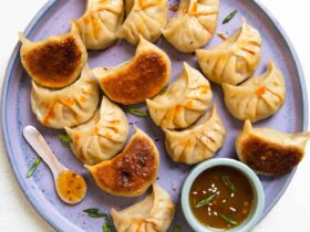 Crispy golden cabbage dumplings arranged on a plate with dipping sauce and fresh scallions
