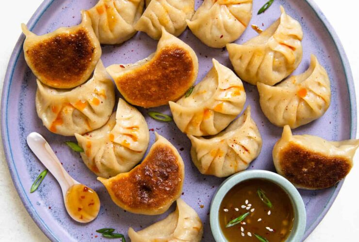 Crispy golden cabbage dumplings arranged on a plate with dipping sauce and fresh scallions