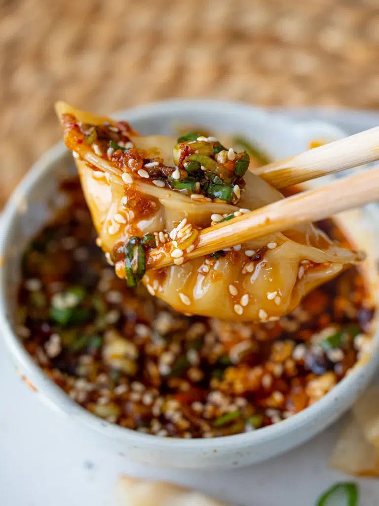 Close-up of dumpling filling ingredients and a folded dumpling mid-pleat on a wooden board