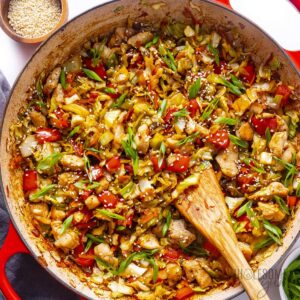 Cabbage stir fry in a hot wok with golden caramelized edges, garlic, ginger, and sesame seeds on a white plate