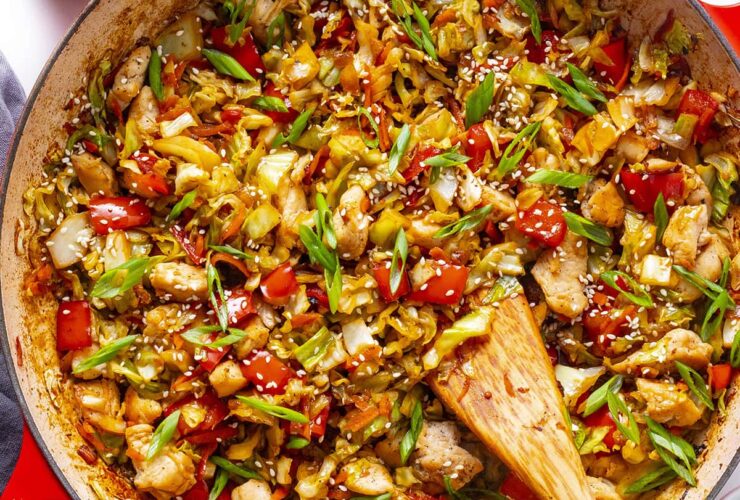 Cabbage stir fry in a hot wok with golden caramelized edges, garlic, ginger, and sesame seeds on a white plate