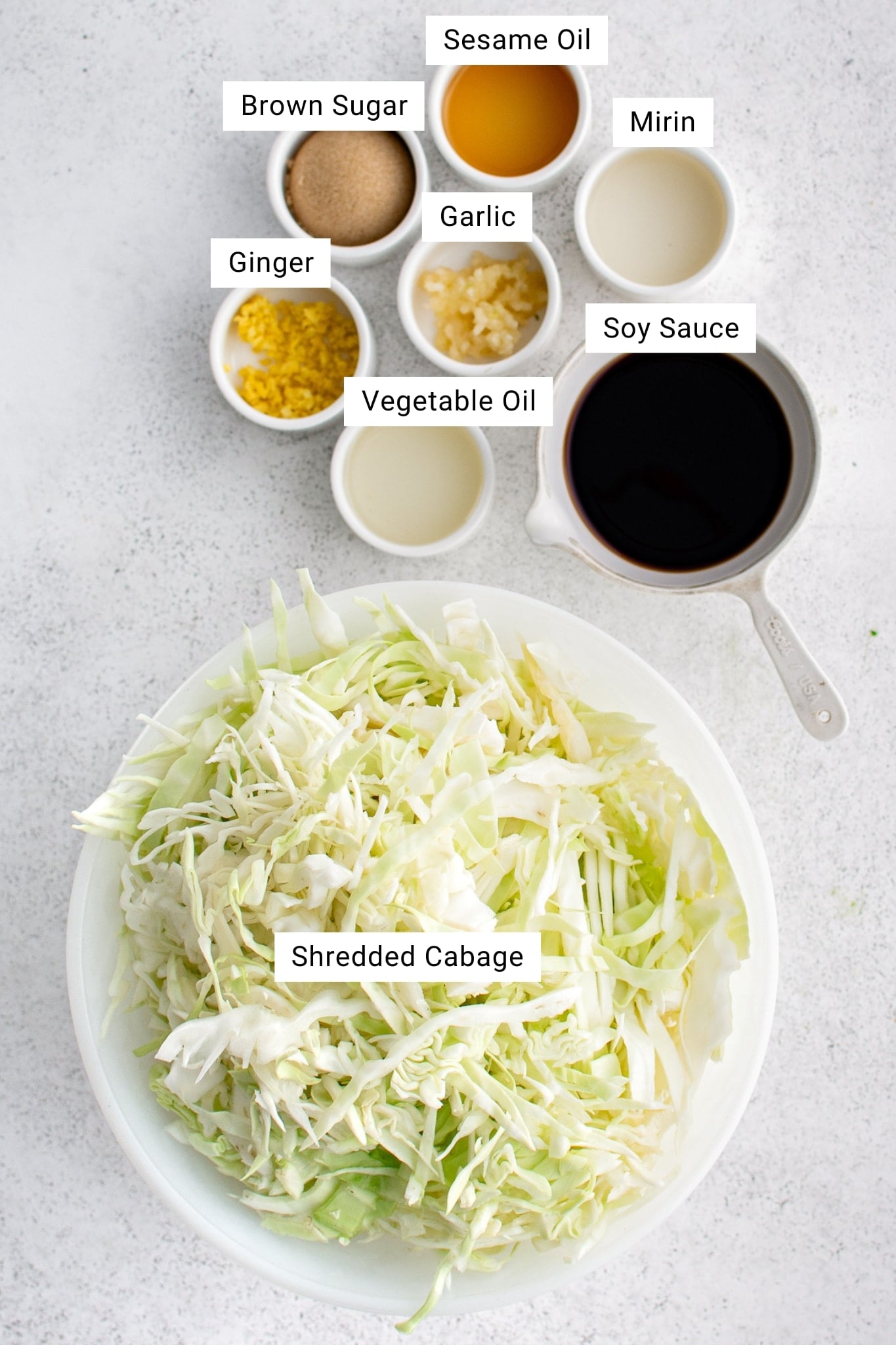 Ingredients for cabbage stir fry laid out on a wooden cutting board — shredded cabbage, minced garlic, grated ginger, soy sauce, sesame oil, and red pepper flakes