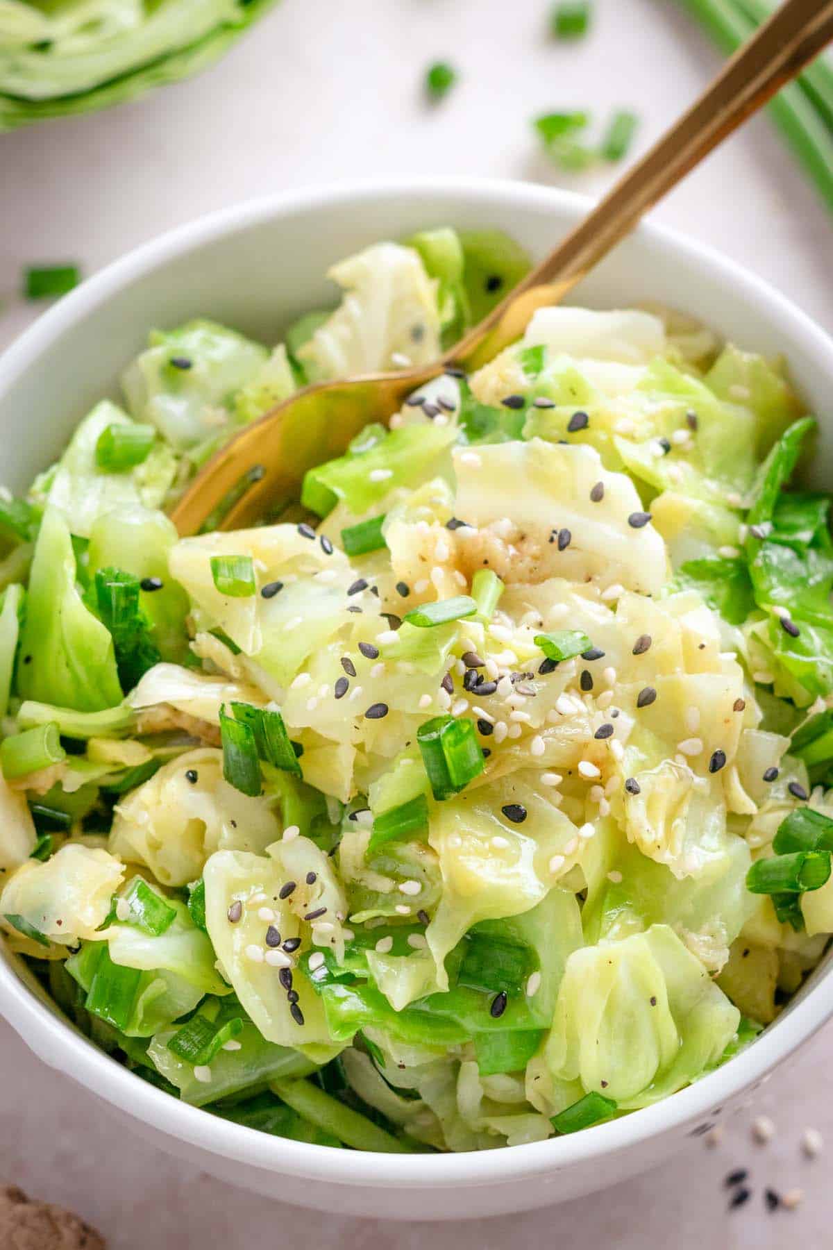 Close-up of cabbage stir fry in a dark bowl topped with sesame seeds, sliced green onions, and a drizzle of sesame oil