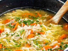 A steaming bowl of from-scratch crockpot chicken noodle soup with golden broth, tender shredded chicken, egg noodles, and fresh parsley, photographed on a rustic wooden table