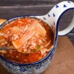 A rustic white bowl filled with golumpki soup — unstuffed cabbage roll soup with ground beef, rice, and tomato broth, garnished with fresh parsley, photographed on a wooden table with a linen napkin