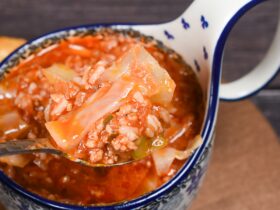 A rustic white bowl filled with golumpki soup — unstuffed cabbage roll soup with ground beef, rice, and tomato broth, garnished with fresh parsley, photographed on a wooden table with a linen napkin