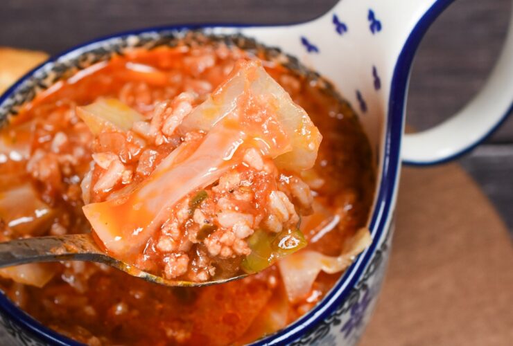 A rustic white bowl filled with golumpki soup — unstuffed cabbage roll soup with ground beef, rice, and tomato broth, garnished with fresh parsley, photographed on a wooden table with a linen napkin