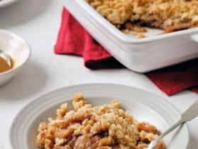 Flat-lay of all key ingredients for greek yogurt apple crisp — sliced apples, rolled oats, sliced almonds, butter cubes, cinnamon sticks, maple syrup, and a bowl of thick Greek yogurt on a marble surface
