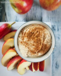 Overhead flat-lay of Greek yogurt caramel apple dip ingredients — yogurt, caramel sauce, cinnamon, vanilla, and sliced apples on a marble surface