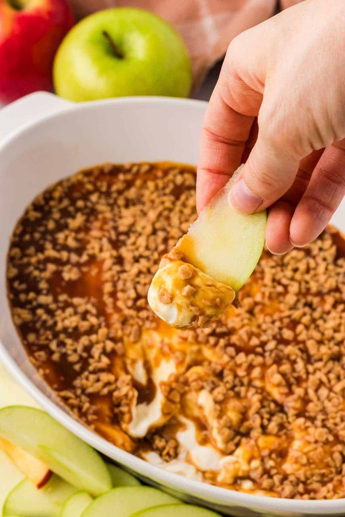 Close-up of an apple slice being dipped into the Greek yogurt caramel apple dip with a golden caramel swirl visible