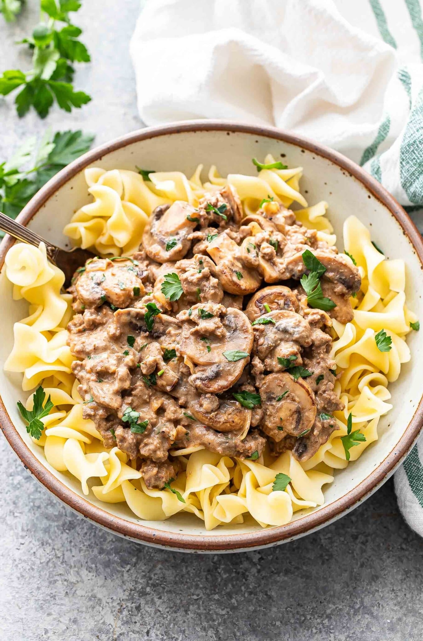 Healthier beef and mushroom skillet served over egg noodles in a white bowl, garnished with fresh parsley