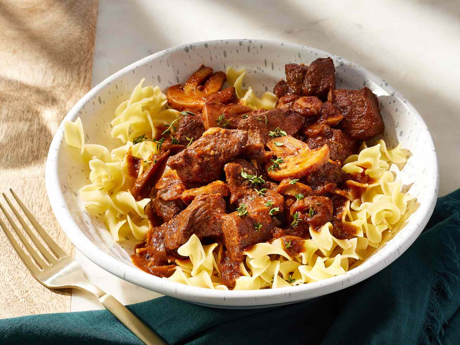 Sliced sirloin tips, halved cremini mushrooms, minced garlic, Greek yogurt, and beef broth arranged on a wooden cutting board