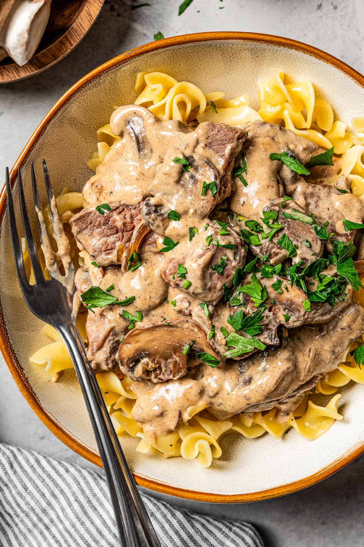Close-up of creamy Greek yogurt beef and mushroom sauce clinging to egg noodles, with fresh parsley and cracked black pepper on top