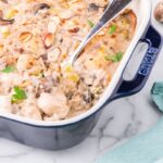 Overhead flat lay of healthier chicken casserole ingredients — raw chicken breast, cremini mushrooms, Greek yogurt, brown rice, broth, garlic, and herbs on a light marble surface