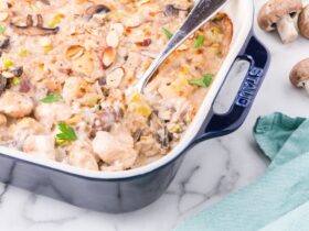 Overhead flat lay of healthier chicken casserole ingredients — raw chicken breast, cremini mushrooms, Greek yogurt, brown rice, broth, garlic, and herbs on a light marble surface