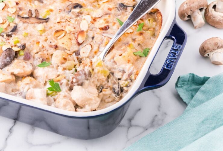 Overhead flat lay of healthier chicken casserole ingredients — raw chicken breast, cremini mushrooms, Greek yogurt, brown rice, broth, garlic, and herbs on a light marble surface