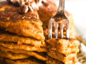 Close-up of a fork cutting into a stack of high protein pumpkin pancakes revealing a fluffy, moist interior, with Greek yogurt and maple syrup dripping down the sides
