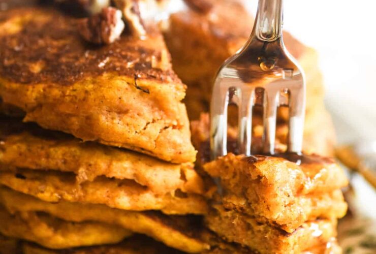 Close-up of a fork cutting into a stack of high protein pumpkin pancakes revealing a fluffy, moist interior, with Greek yogurt and maple syrup dripping down the sides