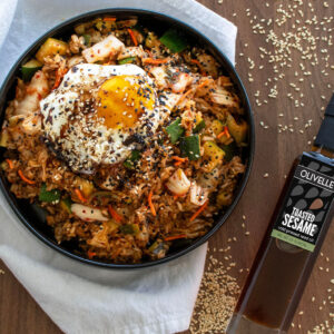 Kimchi Fried Rice — Fermented Cabbage Fried Rice Topped with a Jammy Egg 13 Kimchi fried rice in a black bowl topped with a jammy halved egg, sesame seeds, sliced scallions, and a drizzle of sesame oil, shot overhead on a dark slate surface