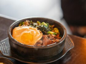 Close-up of a halved jammy egg resting on top of kimchi fried rice, the golden yolk just beginning to ooze, with visible kimchi pieces, sesame seeds, and a scattering of thinly sliced scallions
