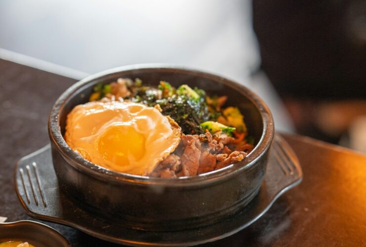 Close-up of a halved jammy egg resting on top of kimchi fried rice, the golden yolk just beginning to ooze, with visible kimchi pieces, sesame seeds, and a scattering of thinly sliced scallions