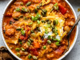 A steaming bowl of lean turkey pumpkin chili topped with sour cream, sliced green onions, and shredded cheese, photographed in warm autumn light