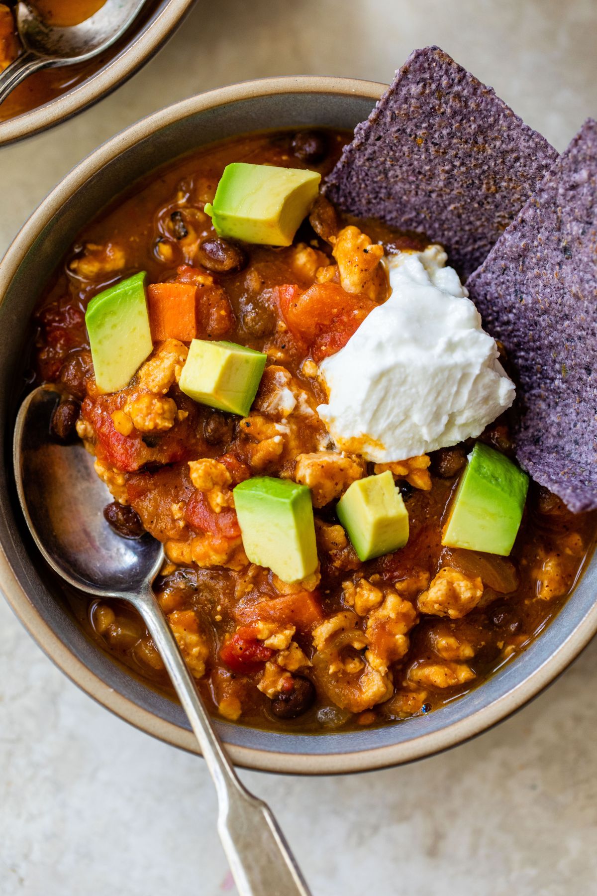 Close-up of a spoonful of lean turkey pumpkin chili being lifted from the bowl, showing rich thick broth, black beans, and tender turkey