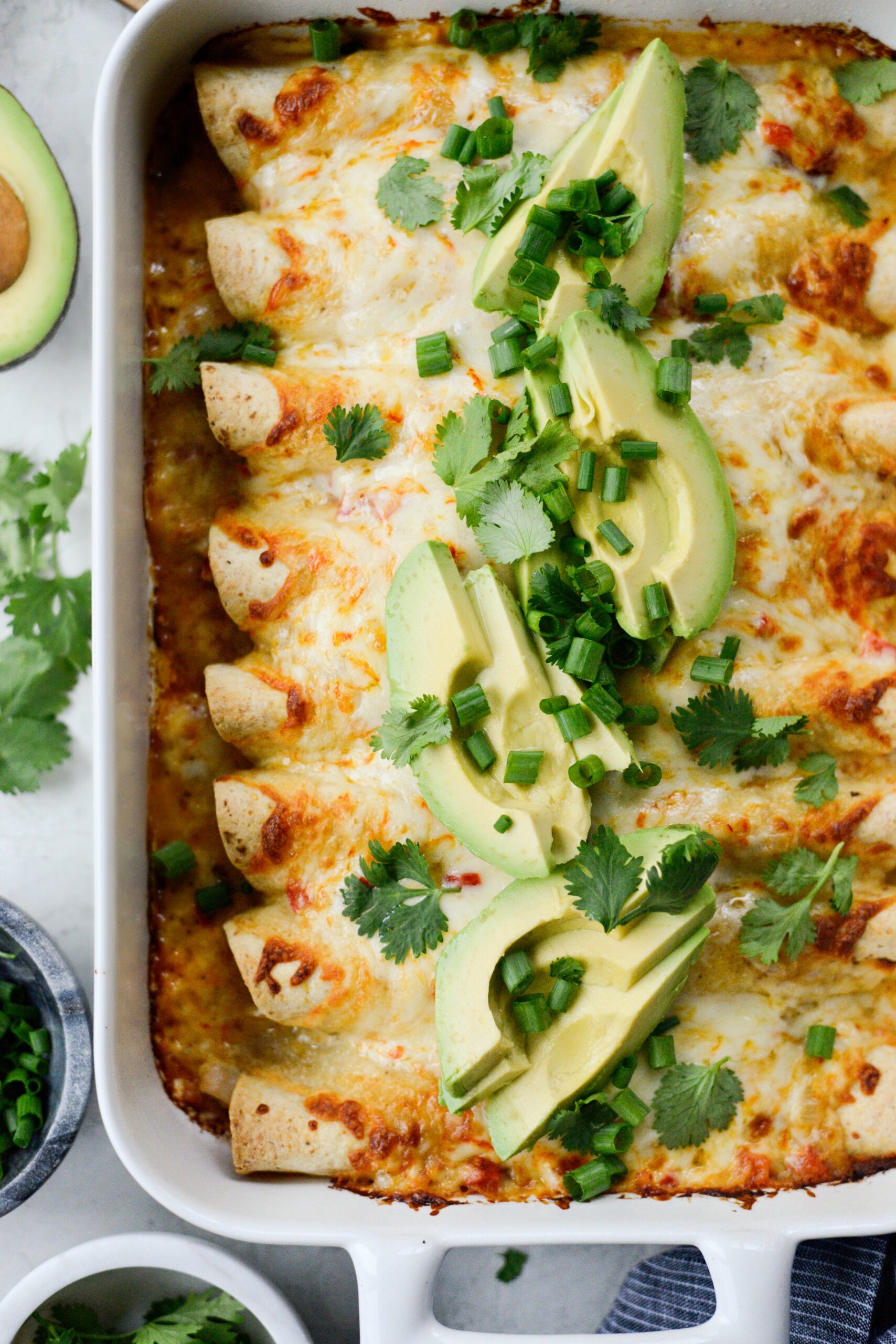 Lightened-up chicken enchiladas fresh from the oven in a baking dish, topped with melted cheese, fresh cilantro, and a dollop of Greek yogurt