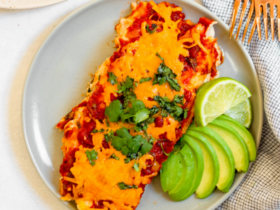 Close-up of a lightened-up chicken enchilada being served, showing the creamy sauce layer, shredded chicken filling, and melted cheese with fresh cilantro garnish