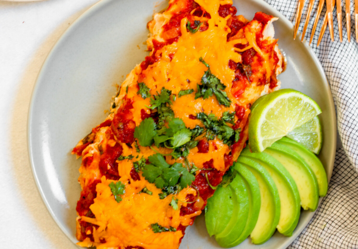 Close-up of a lightened-up chicken enchilada being served, showing the creamy sauce layer, shredded chicken filling, and melted cheese with fresh cilantro garnish